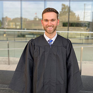 Andrew Horne in graduation robe standing in front of the CIGI building