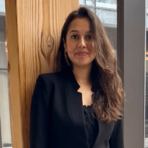 A young woman standing in front of a wood beam smiling at the camera.